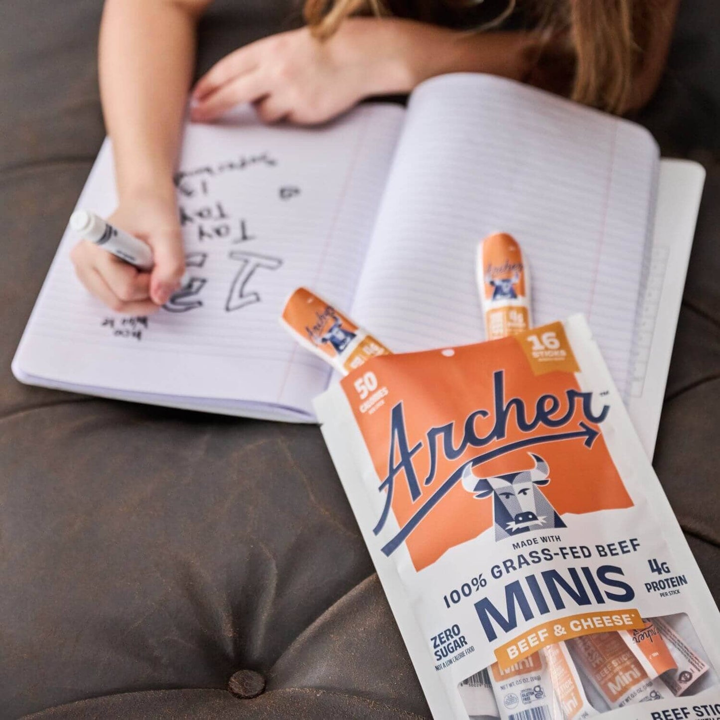 Archer Beef and Cheese Mini Sticks laying on a couch next to a child drawing